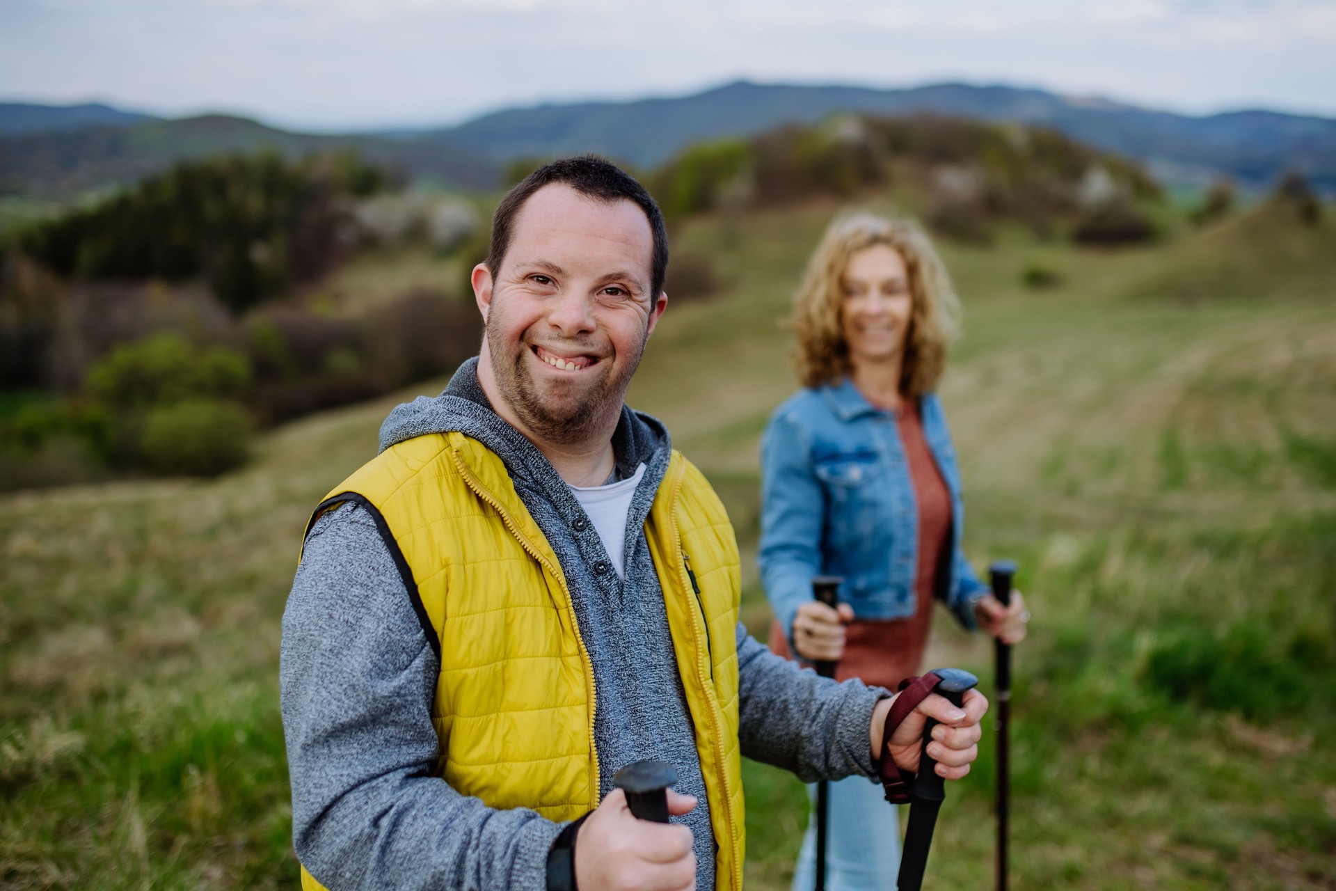 Portrait of happy young man with Down syndrome with his mother hiking together in nature.