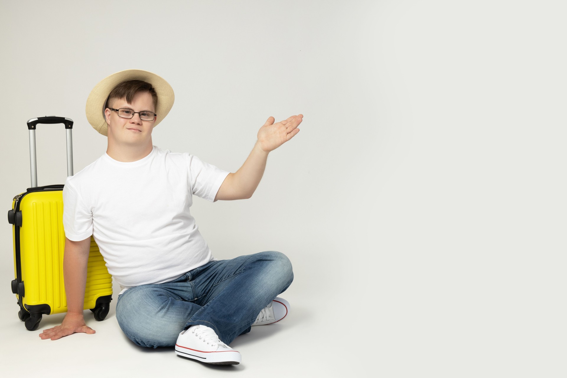 Smiling young man with down syndrome in glasses with suitcase and hat