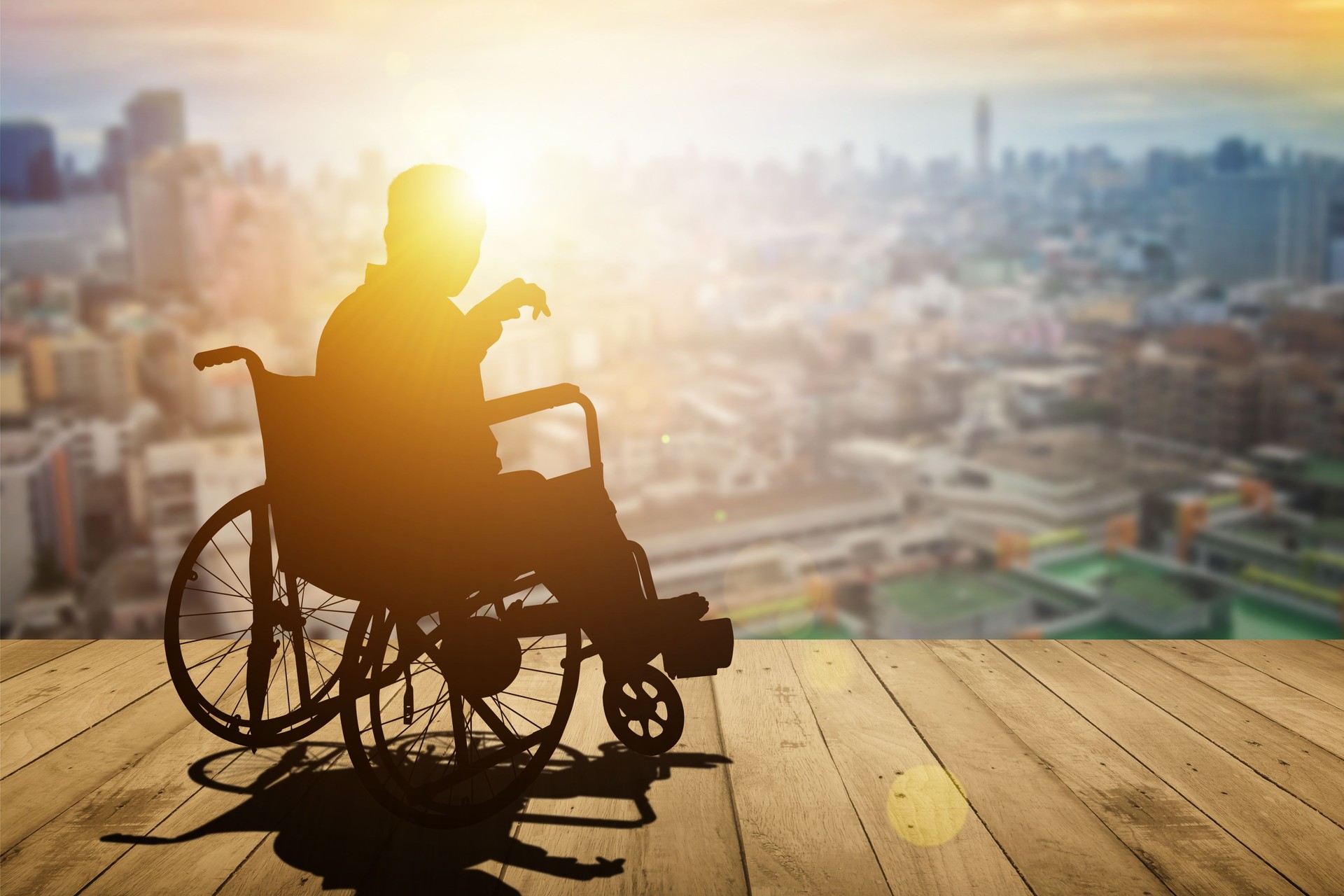 Disabled person silhouette with hand lift on wheelchair have sunset city background. International Disability Day or Handicapped sport or Paralympics. Challenge and Conquer success and health concept.
